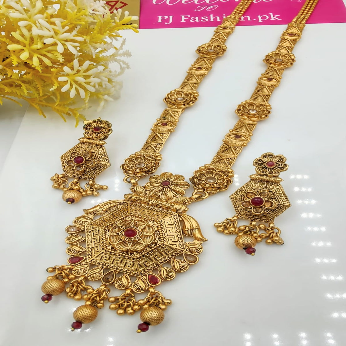 Gold necklace and earrings set with red stones on a white background, branded 'FJ Fashion.pk'.